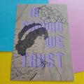 An art print featuring a black ink illustration of a woman in profile with flowers and the text 'IN SAPPHO WE TRUST' in lavender, placed on a background split into blue, pink, and yellow sections.