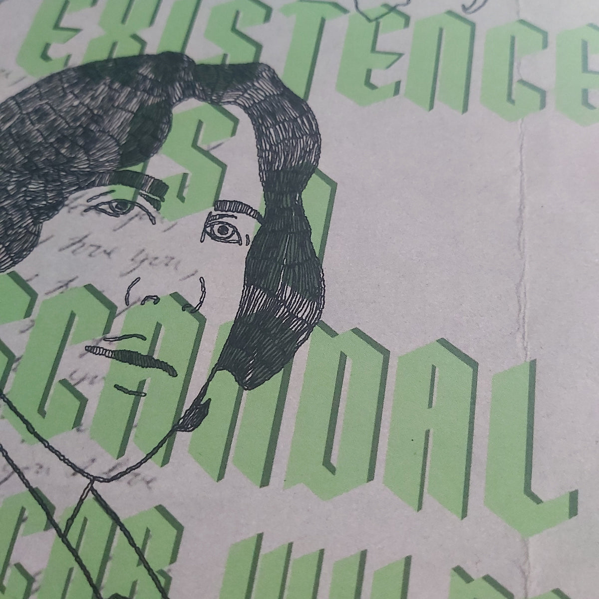 A close-up of a printed artwork featuring a black ink sketch of a face layered over large light green stylised text on a beige background.