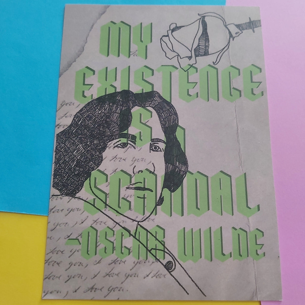An art print featuring a black ink illustration of Oscar Wilde with the title 'MY EXISTENCE IS A SCANDAL -OSCAR WILDE' in large green letters, displayed on a colourful background of yellow, pink, and blue paper.