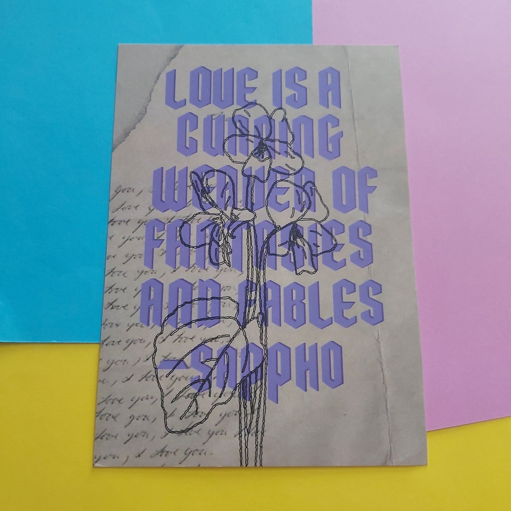 An art print featuring a quote by Sappho in lavender-purple text over a beige background with cursive script and a flower illustration, displayed on a colourful background of blue, pink, and yellow paper.