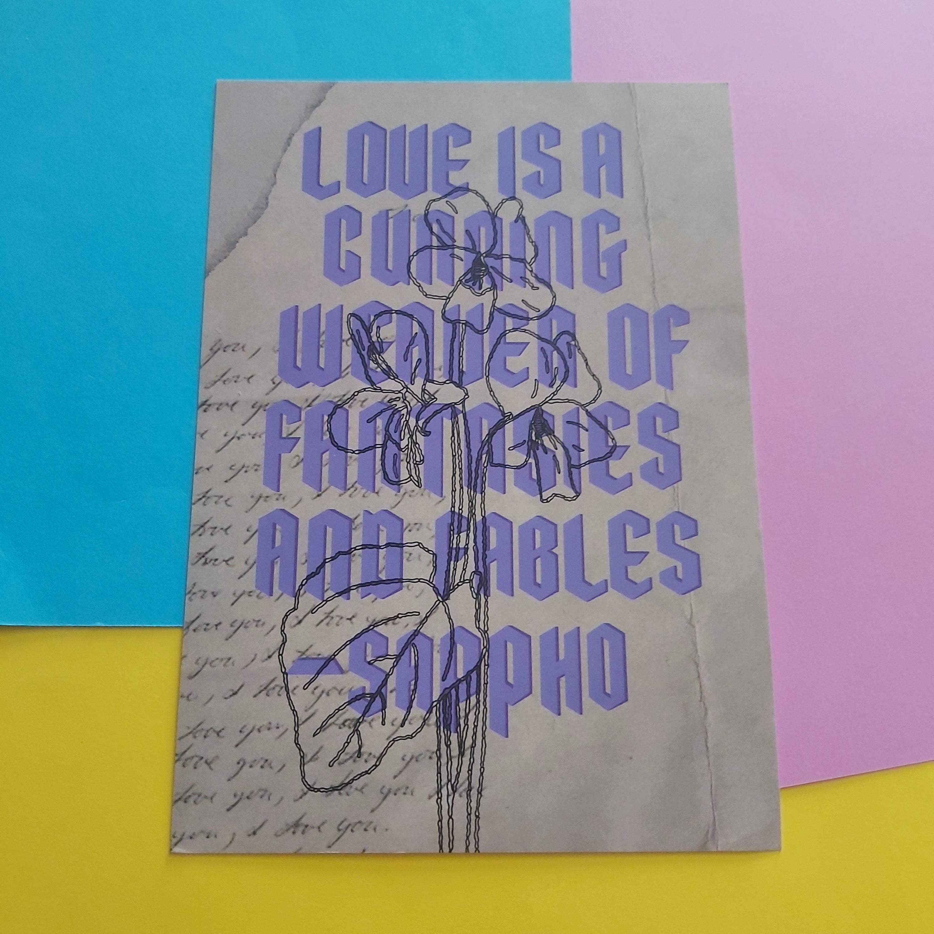 An art print featuring a quote by Sappho in lavender-purple text over a beige background with cursive script and a flower illustration, displayed on a colourful background of blue, pink, and yellow paper.