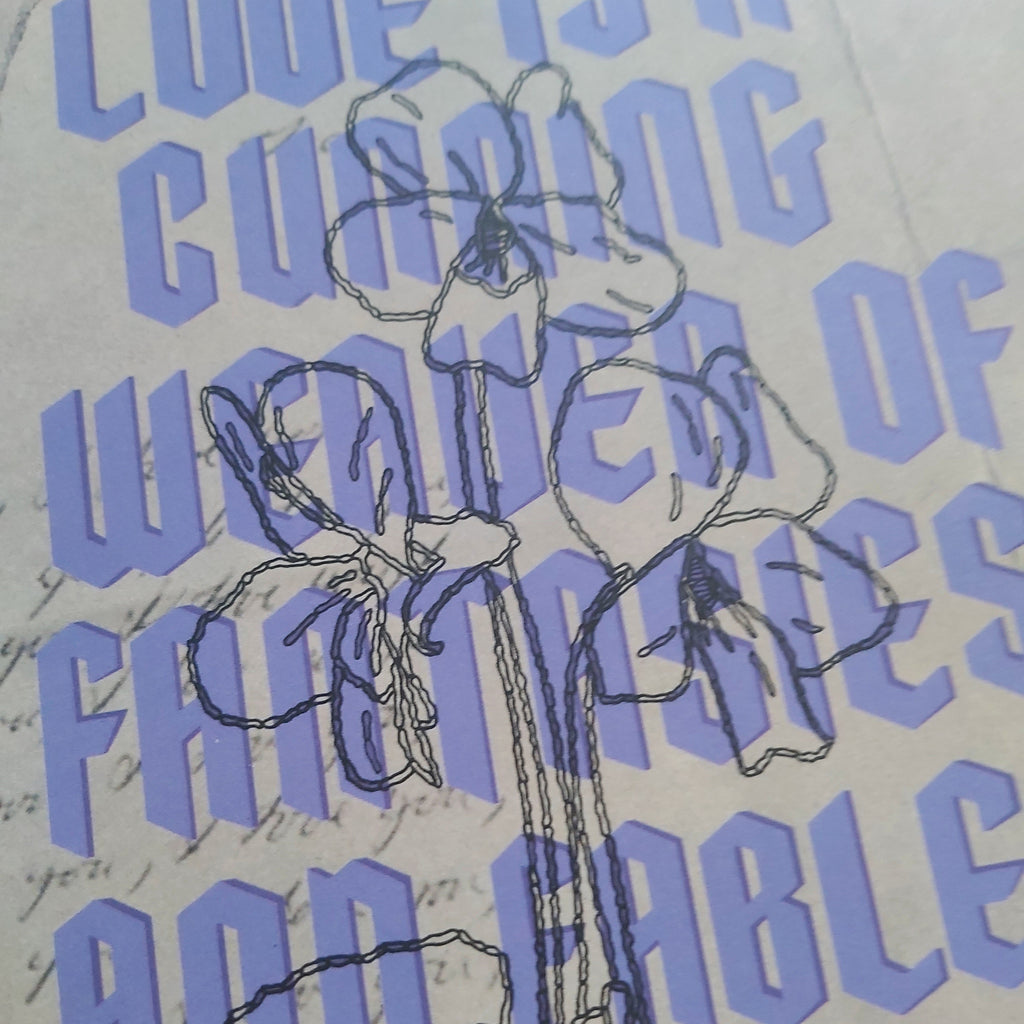A close-up of a printed design featuring a black line-art sketch of flowers over a background of light purple text reading 'LOVE IS A CUNNING WEAVER OF FANTASIES AND FABLES' on a cream-colored paper.