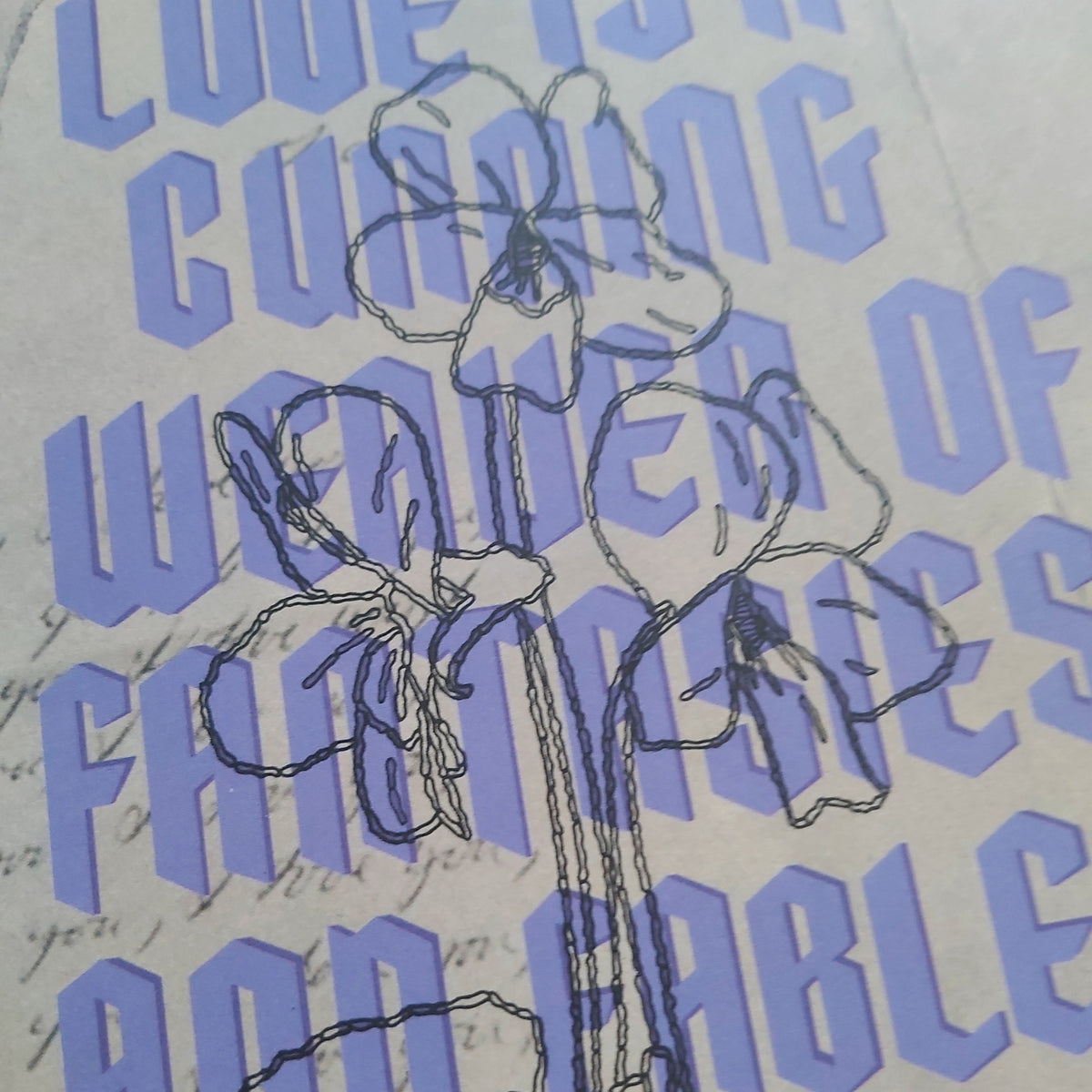 A close-up of a printed design featuring a black line-art sketch of flowers over a background of light purple text reading 'LOVE IS A CUNNING WEAVER OF FANTASIES AND FABLES' on a cream-colored paper.
