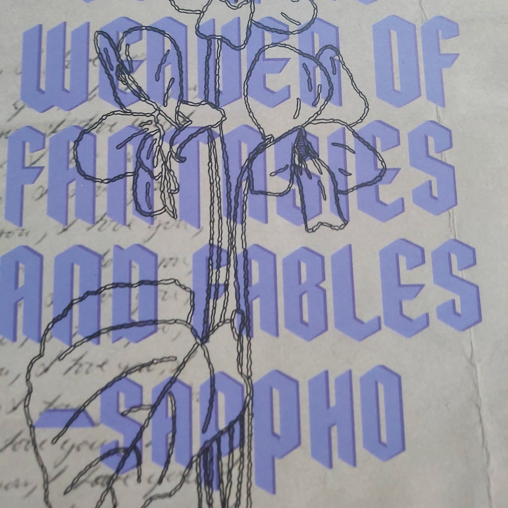 A close-up of a print design featuring large lavender text reading 'Love is a cunning weaver of fantasies and fables -Sappho' over a cream background, with a black line drawing of a flower and leaf motif.