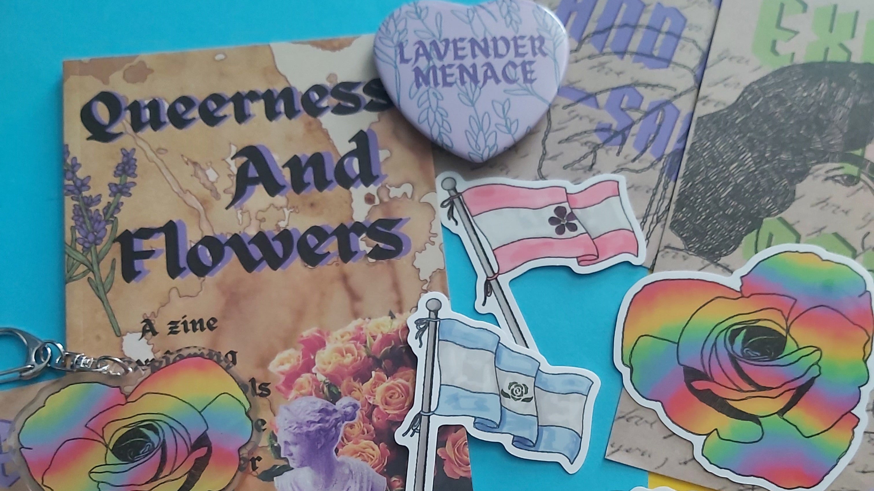 A flat lay of colorful stickers and pins featuring lavender-themed designs, including a heart-shaped pin that reads 'Lavender Menace,' a sticker that says 'Pansy Club Member,' and rainbow-colored rose stickers on a bright blue, yellow, and brown collage background.
