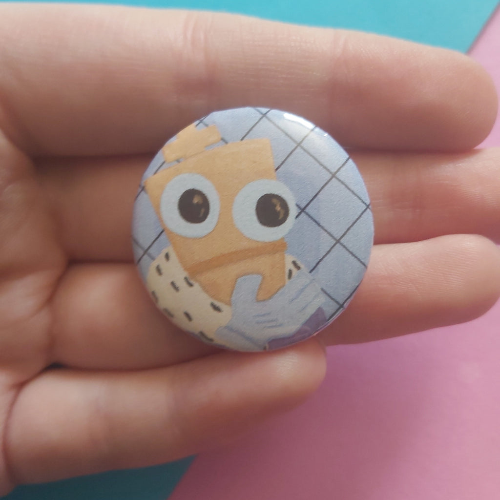 A round pinback button badge featuring a cartoon character with large eyes, held in a person's hand against a split blue and pink background.