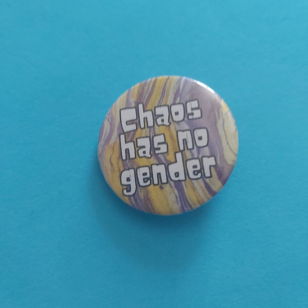 A round pinback button with a marbled yellow, purple, and white background and the text 'Chaos has no gender' in white bubble letters, shown on a solid turquoise blue background.