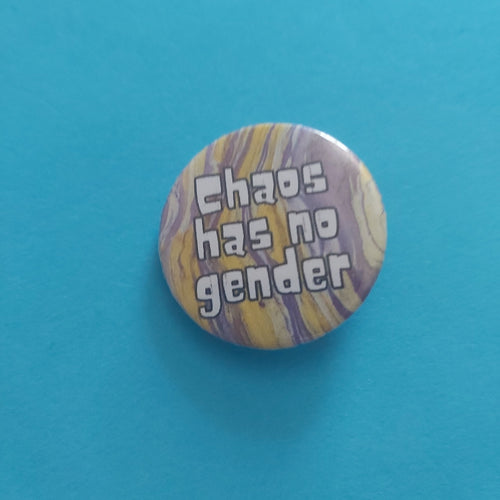 A round pinback button with a marbled yellow, purple, and white background and the text 'Chaos has no gender' in white bubble letters, shown on a solid turquoise blue background.