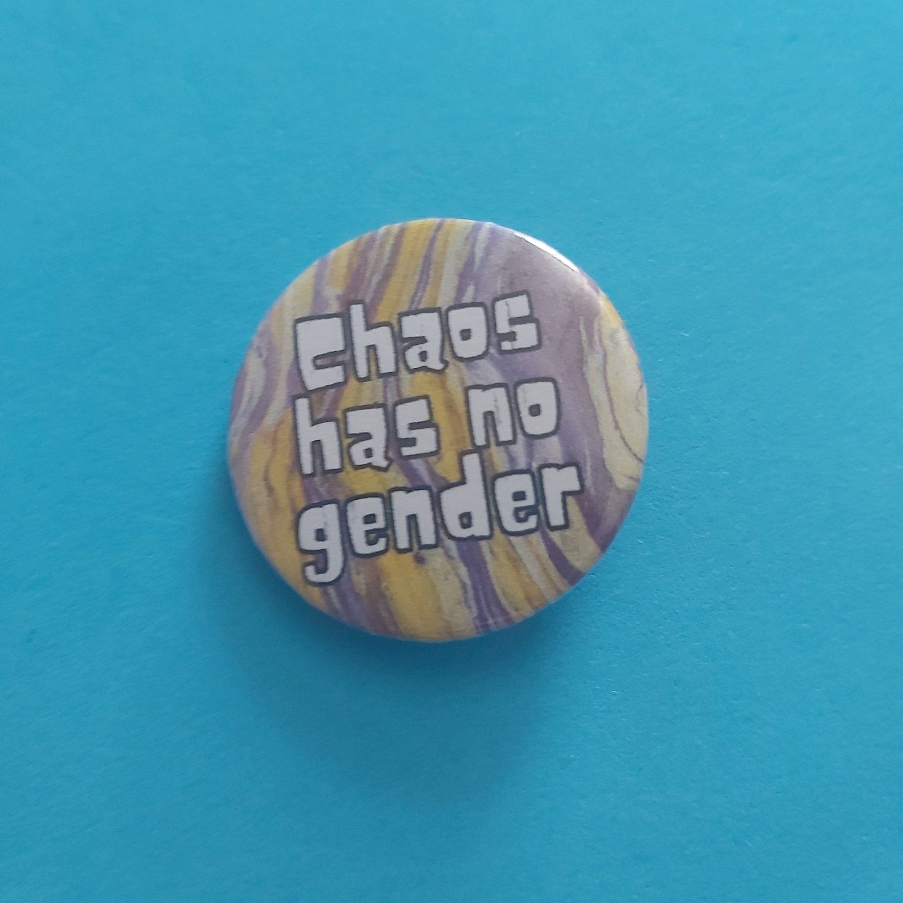 A round pinback button with a yellow and purple marbled pattern and the text 'Chaos has no gender' in white bubble letters, set against a solid bright blue background.