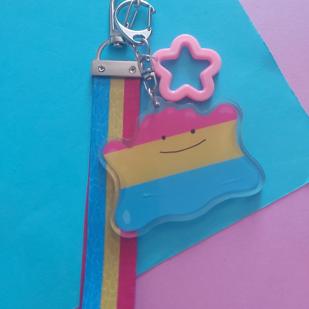 A keychain featuring a Pan Pride flag charm, a pink star-shaped accent, and a silver lobster clasp, displayed on a colourful geometric paper background.