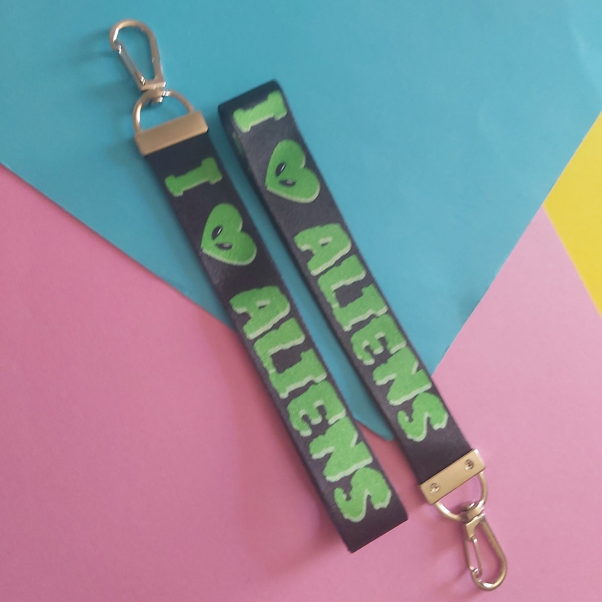 A black leather wristlet strap keychain featuring the text 'I <3 ALIENS' in green with a green alien head heart, displayed on a colorful pink, blue, and yellow background.