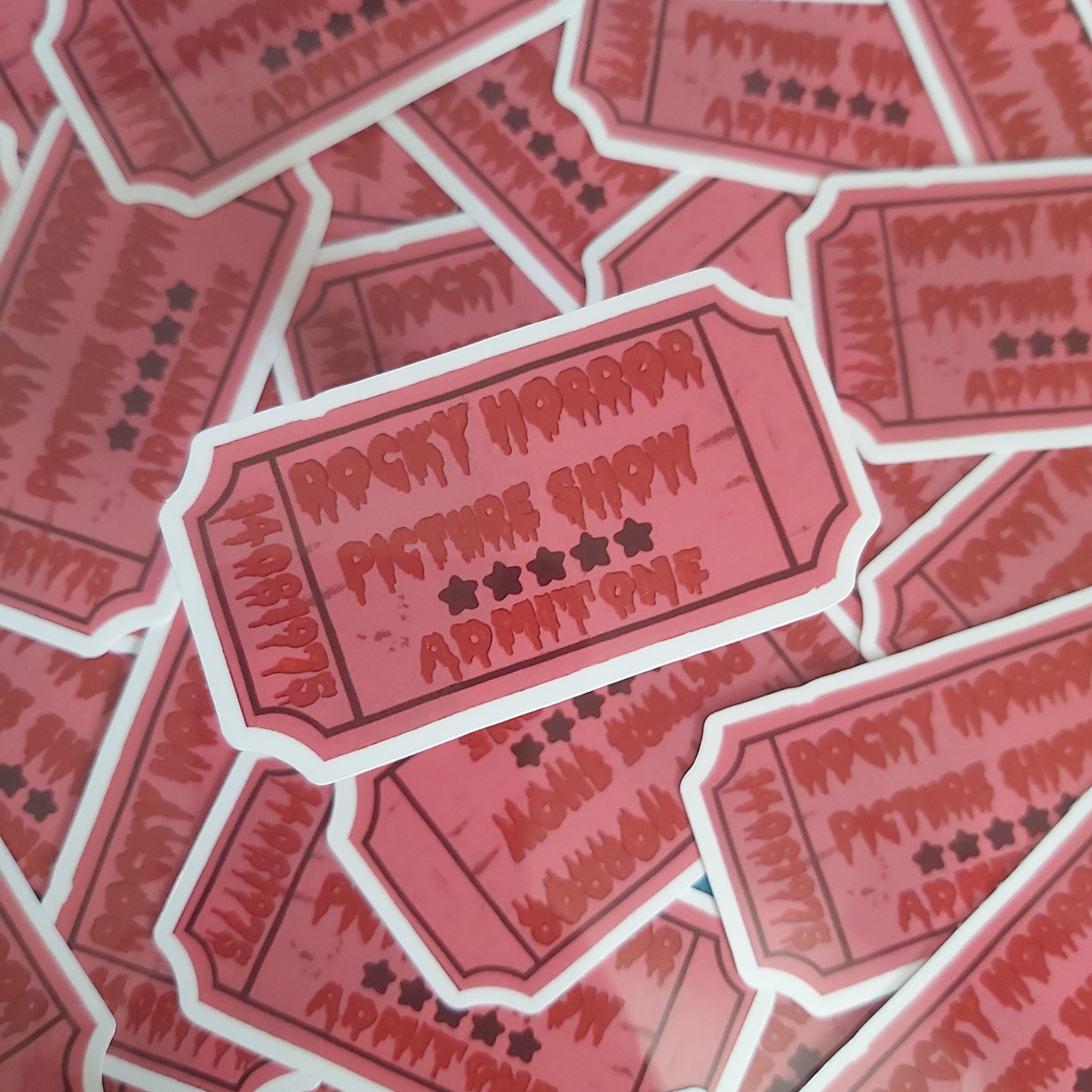 A pile of die-cut stickers shaped like vintage movie ticket stubs in pink and red tones, printed with the text 'Rocky Horror Picture Show Admit One' and small black stars.