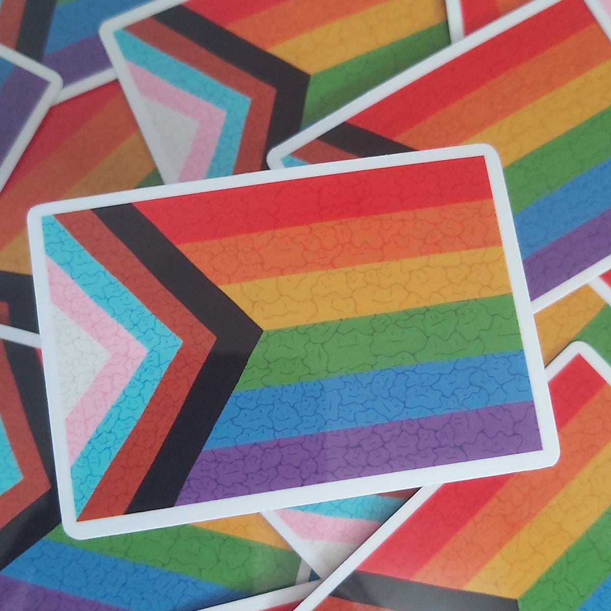 A pile of rectangular stickers featuring a chevron-style rainbow design with horizontal rainbow stripes and a white border.