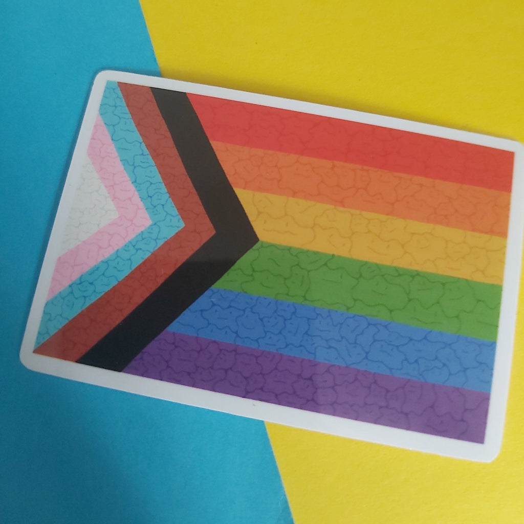 A rectangular card featuring the Progress Pride flag design with ditto face texture, resting on a diagonally split yellow and blue background.