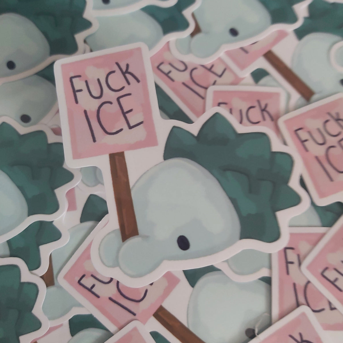 A pile of die-cut stickers featuring a cute Pokémon holding a sign that reads 'Fuck ICE' in black handwritten-style text.