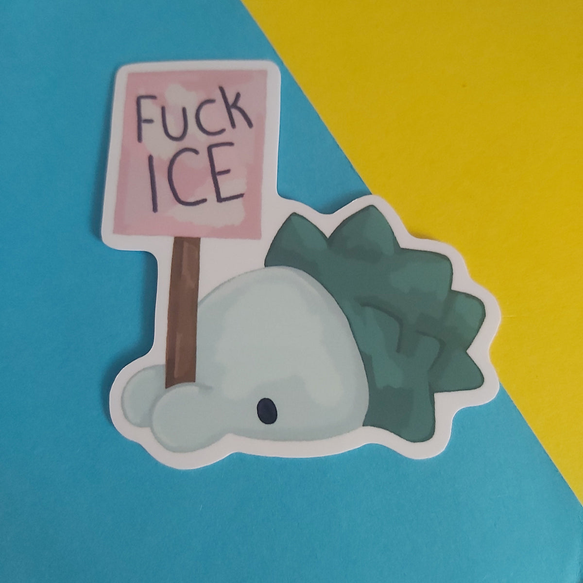 A die-cut sticker featuring a Pokémon called Snom holding a pink sign that reads 'FUCK ICE' in black handwritten text. The sticker is displayed on a diagonally split blue and yellow background.