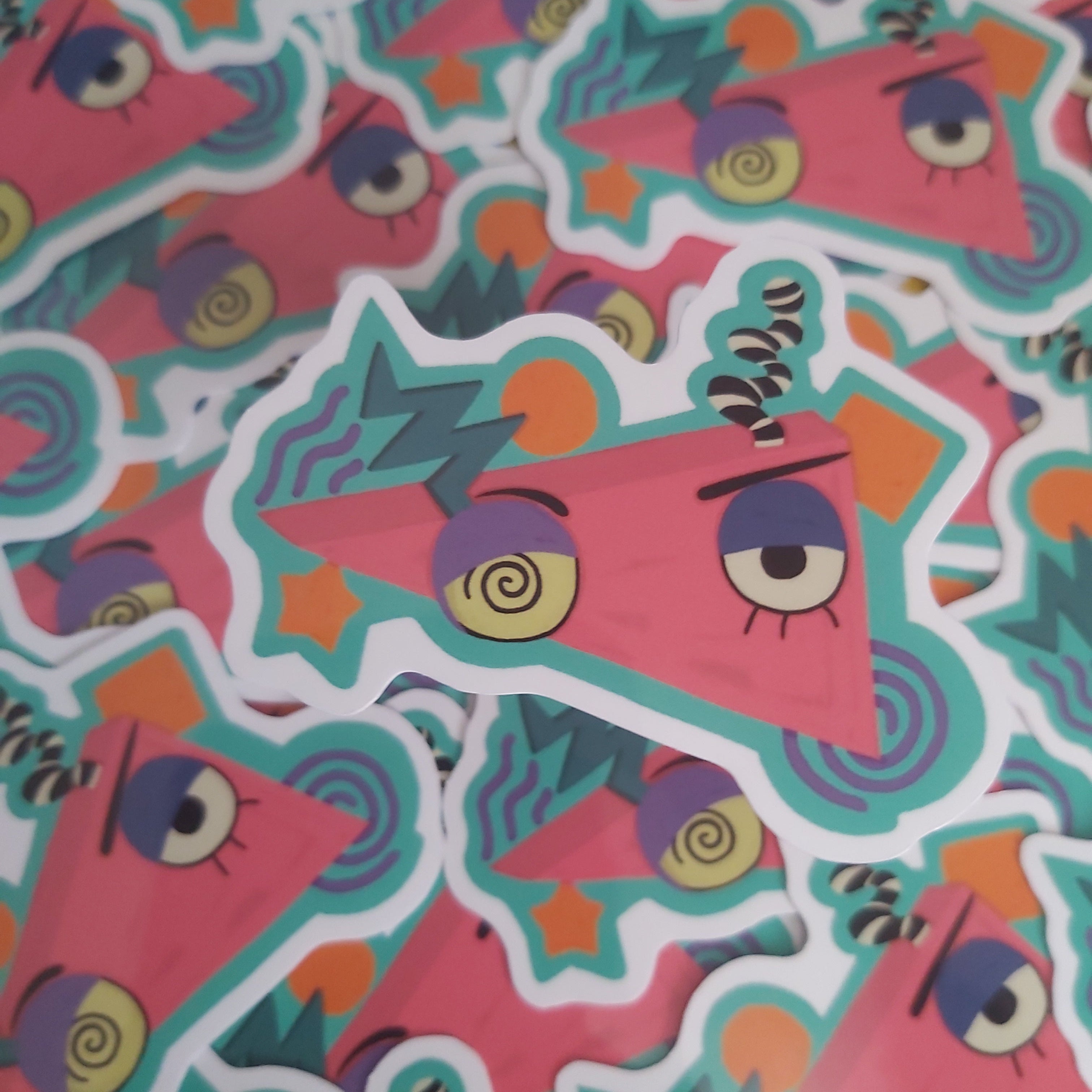 A pile of colourful cartoon stickers featuring a pink triangular character with purple spiral eyes, yellow stars, and teal wavy outlines.