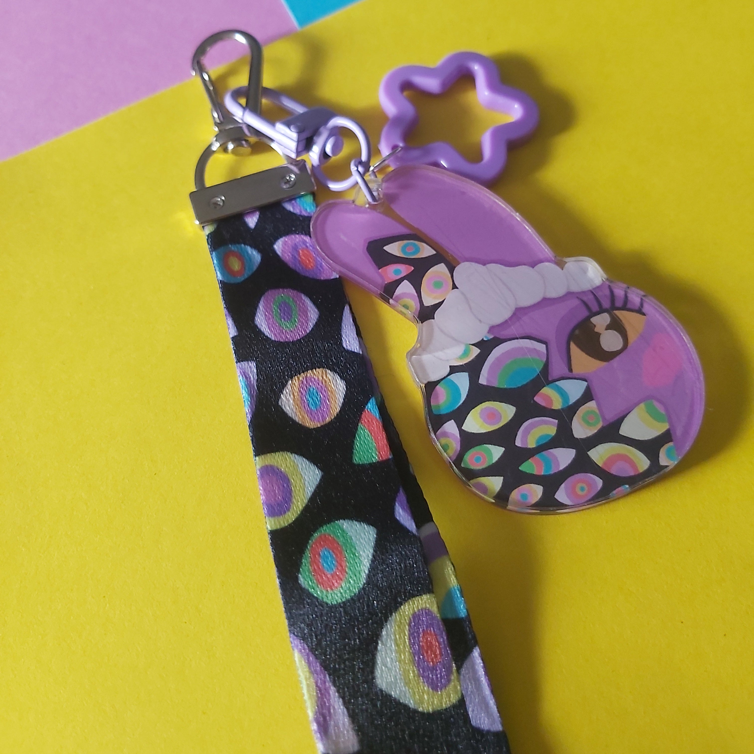 A purple and black patterned keychain bag with a silver clasp, resting on a colorful background of yellow, pink, and blue paper.