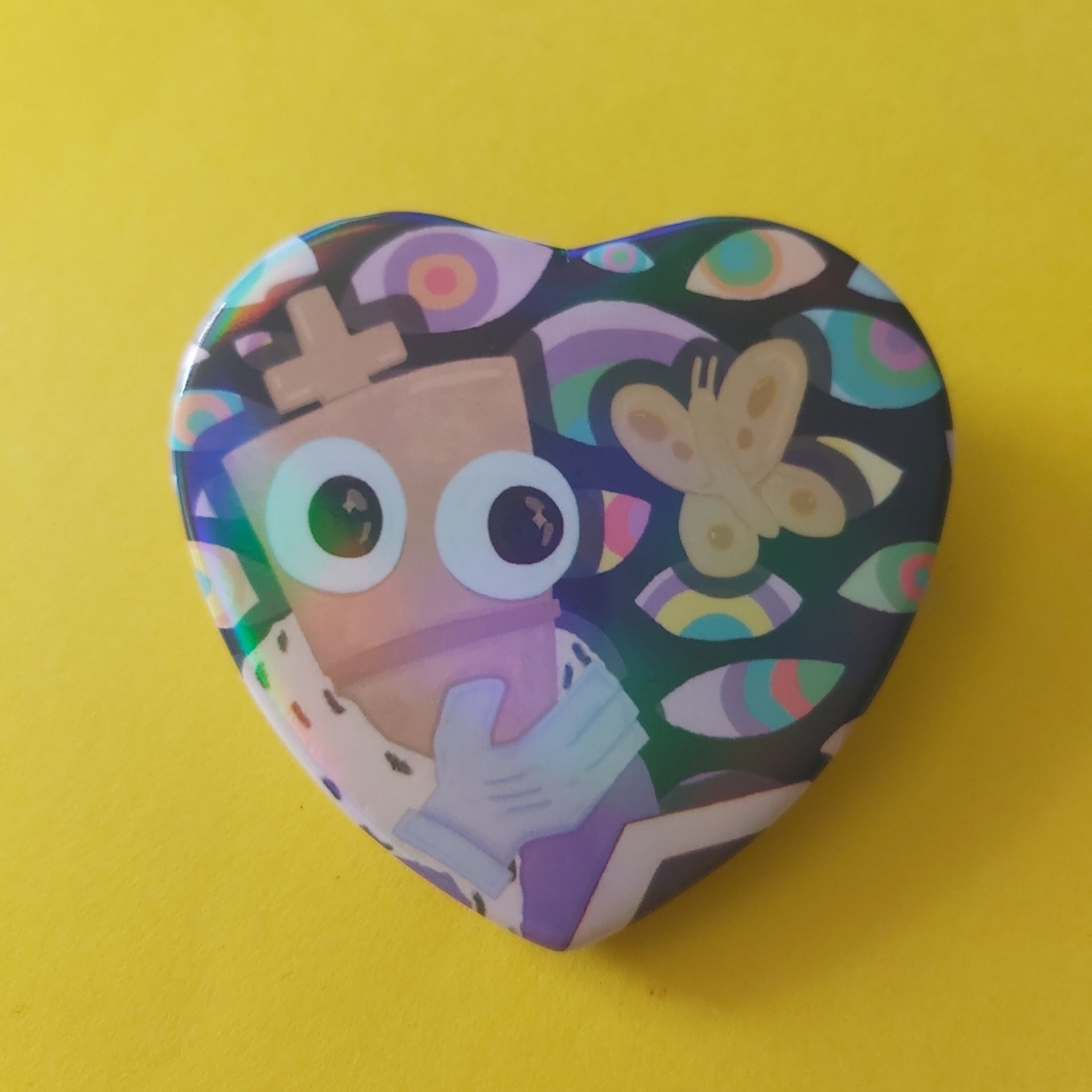 A heart-shaped pinback button featuring a colourful chess piece character illustration of a character with large eyes and a butterfly on a dark background, set against a solid yellow backdrop.