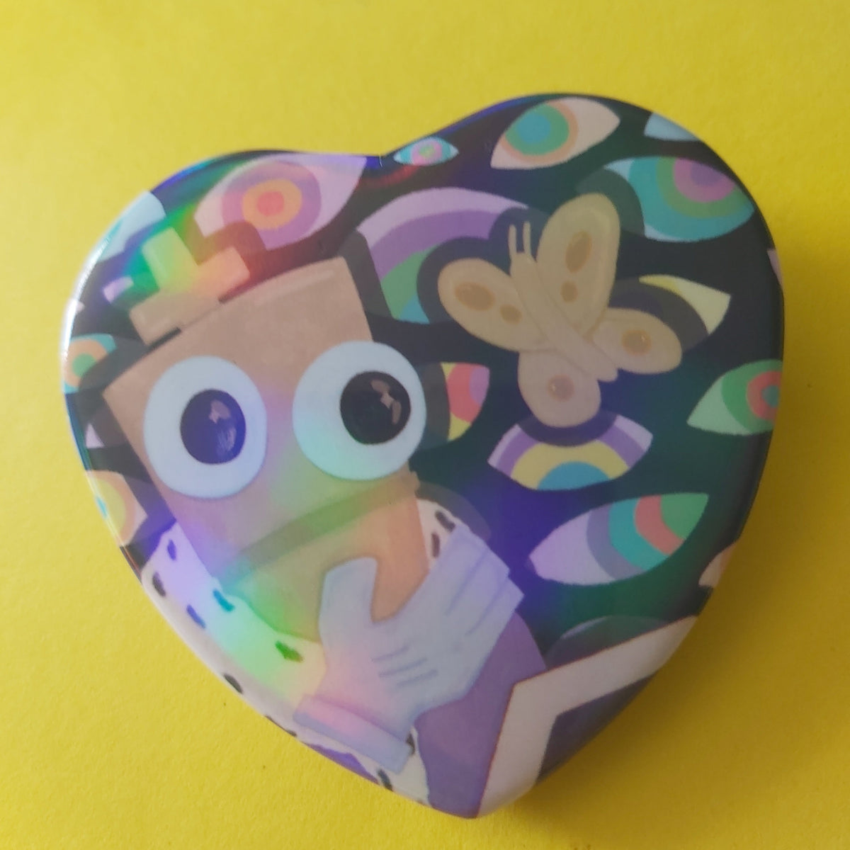 A heart-shaped glossy pinback button featuring a colourful, iridescent holographic design with a chess piece character cartoon eyes and a butterfly, set against a solid yellow background.