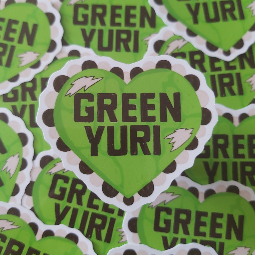 A pile of die-cut heart-shaped stickers featuring the text 'GREEN YURI' in black lettering on a bright lime green background, with a white and black scalloped lace border and small white lightning bolt accents.