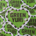 A pile of die-cut heart-shaped stickers featuring the text 'GREEN YURI' in black lettering on a bright lime green background, with a white and black scalloped lace border and small white lightning bolt accents.