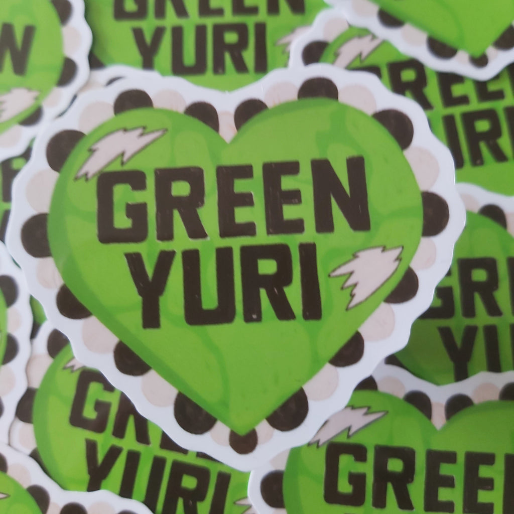 A pile of die-cut heart-shaped stickers featuring the text 'GREEN YURI' in bold black letters on a bright lime green background, with a white scalloped border and small lightning bolt accents.