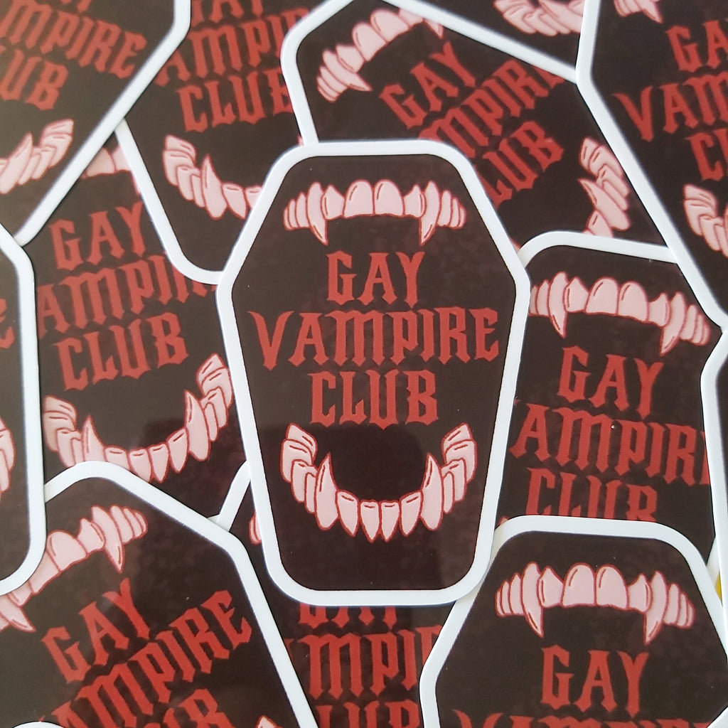 A pile of die-cut stickers featuring a dark brown coffin-shaped design with the words 'GAY VAMPIRE CLUB' in red and a vampire mouth graphic with white teeth.
