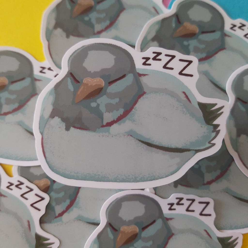 A pile of die-cut stickers featuring a cartoon sleeping pigeon with 'ZZZ' text, shown on a colorful background of yellow, pink, and blue paper.