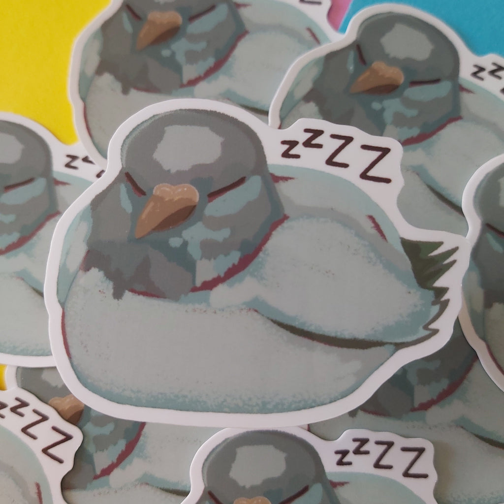 A close-up of several die-cut stickers featuring a sleeping grey pigeon bird with 'ZZZ' text, arranged on a colourful background of yellow, pink, and blue shapes.
