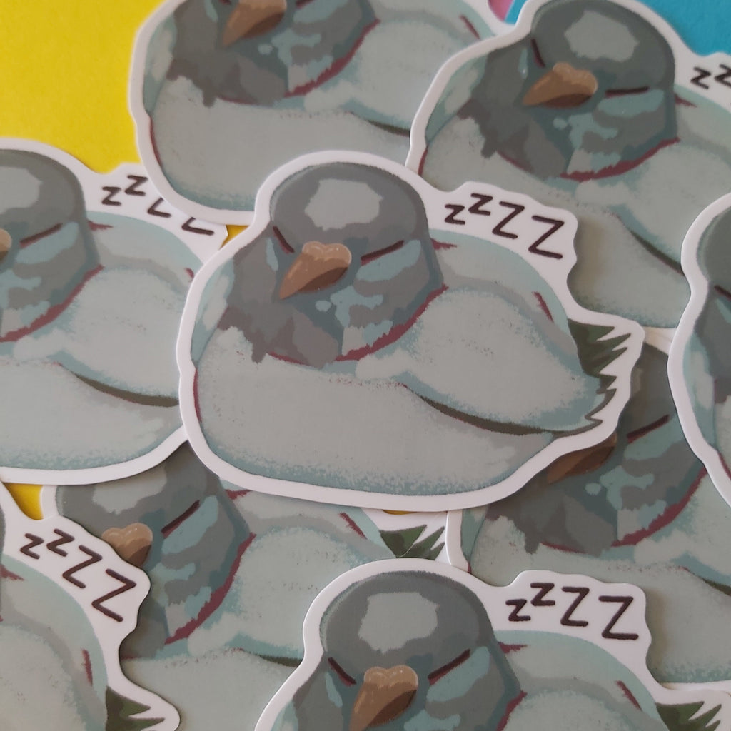 A pile of die-cut stickers featuring cartoon sleeping pigeons with 'zzzz' text, shown on a colorful background of yellow, pink, and blue paper.