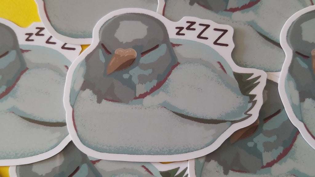 A pile of die-cut stickers featuring a sleeping grey pigeon bird with 'zzzz' text, arranged on a colourful background of yellow, pink, and blue.