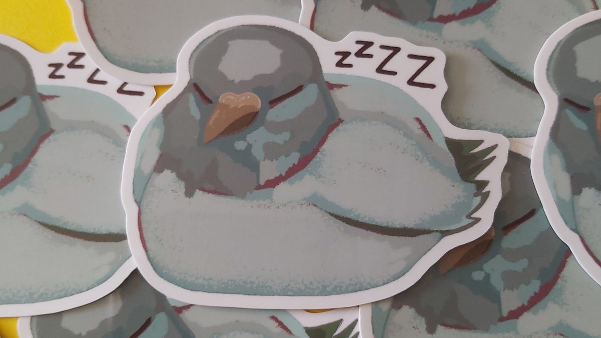 A pile of die-cut stickers featuring a sleeping grey pigeon bird with 'zzzz' text, arranged on a colourful background of yellow, pink, and blue.