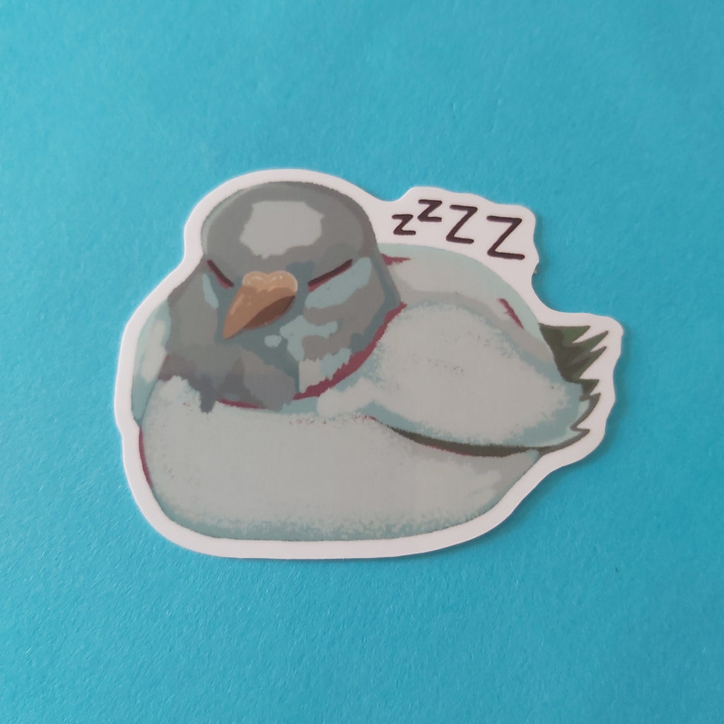 A die-cut sticker of a sleeping grey pigeon bird with 'ZZZ' text above it, placed on a bright blue background.