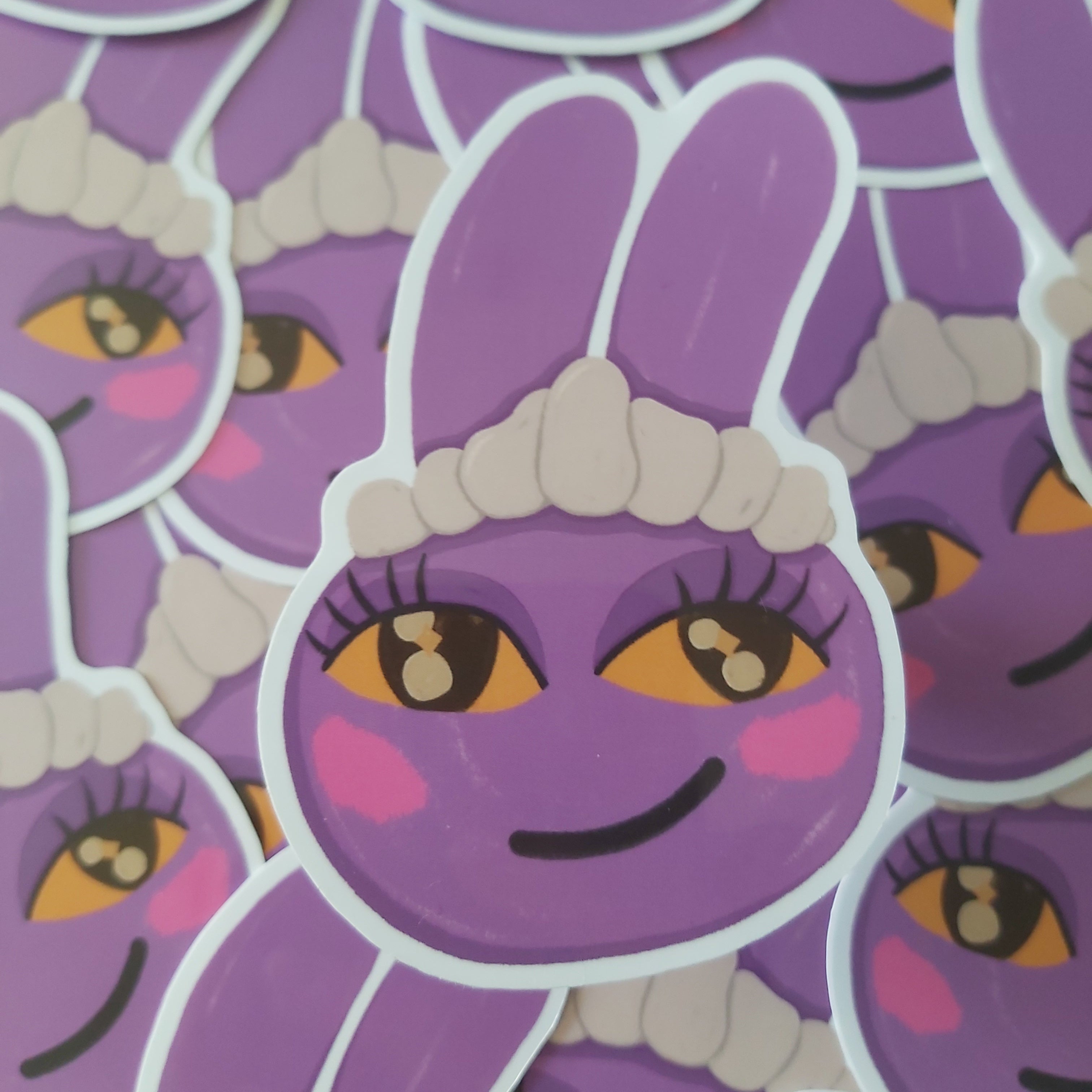 A close-up of multiple die-cut stickers featuring a purple cartoon bunny Jax character with large yellow eyes, pink cheeks, and a white maid hat, layered over one another.