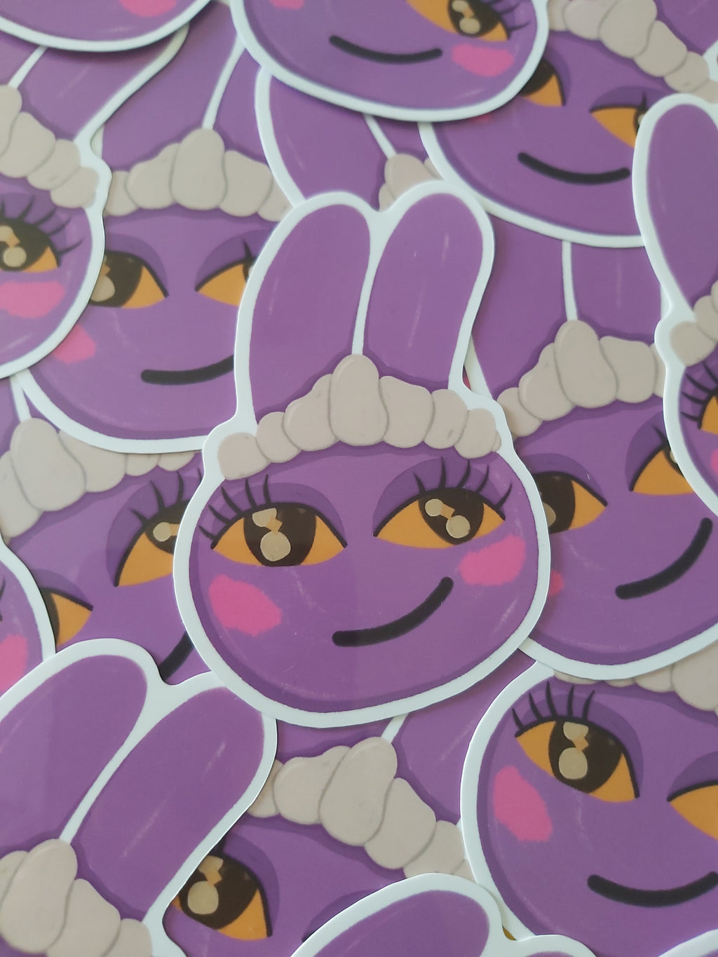 A close-up of a pile of die-cut stickers featuring a purple cartoon bunny called Jax from The Amazing Digital Circus with yellow eyes, pink cheeks, and a white maid hat.