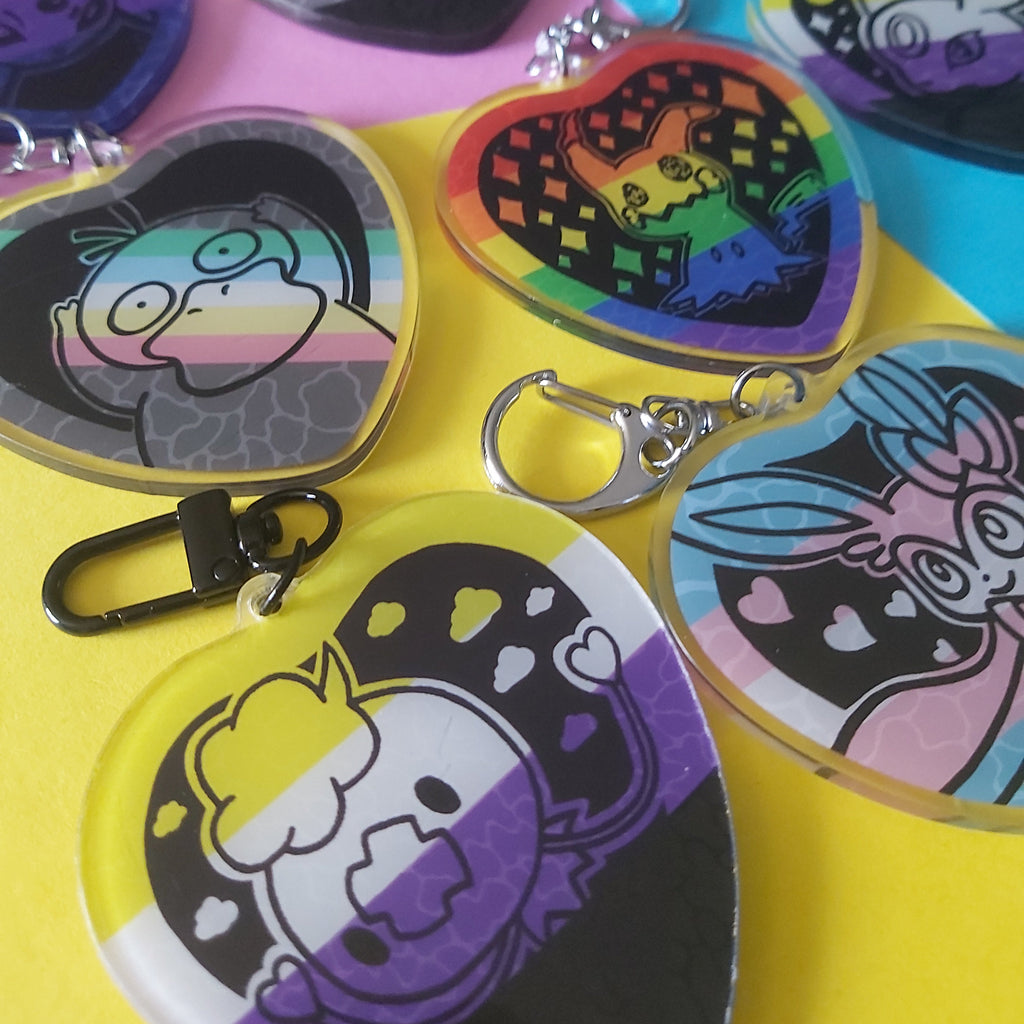A collection of heart-shaped acrylic keychains featuring colorful cartoon character illustrations, displayed on a bright yellow and pink background.