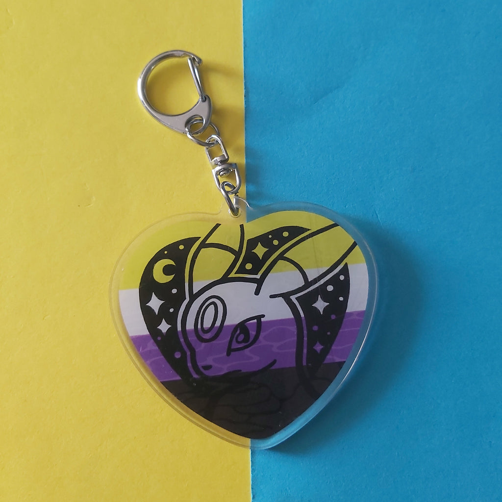 A heart-shaped acrylic keychain featuring an Umbreon Pokémon character illustration with a black, white, yellow, and purple non-binary flag design, attached to a silver lobster clasp, set against a split yellow and blue background.