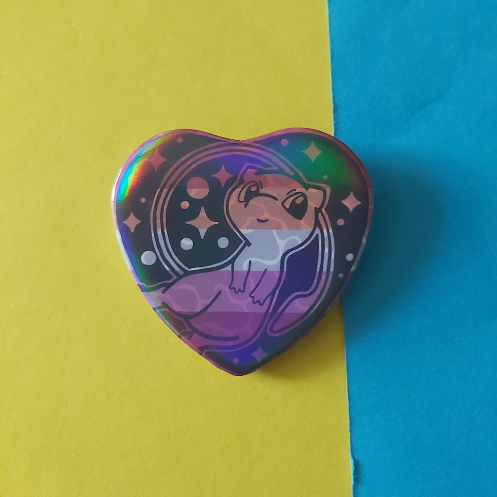 A heart-shaped holographic pin featuring a cute cartoon on a lesbian flag, resting on a split yellow and blue background.