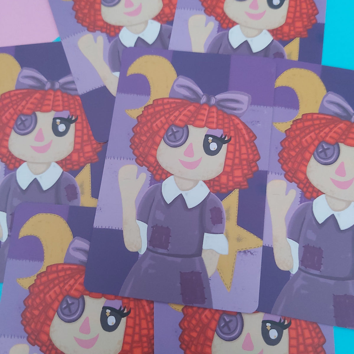 A close-up of several overlapping printed cards featuring a cartoon girl with red curly hair, purple clothing, and a purple bow, arranged on a pink and blue background.