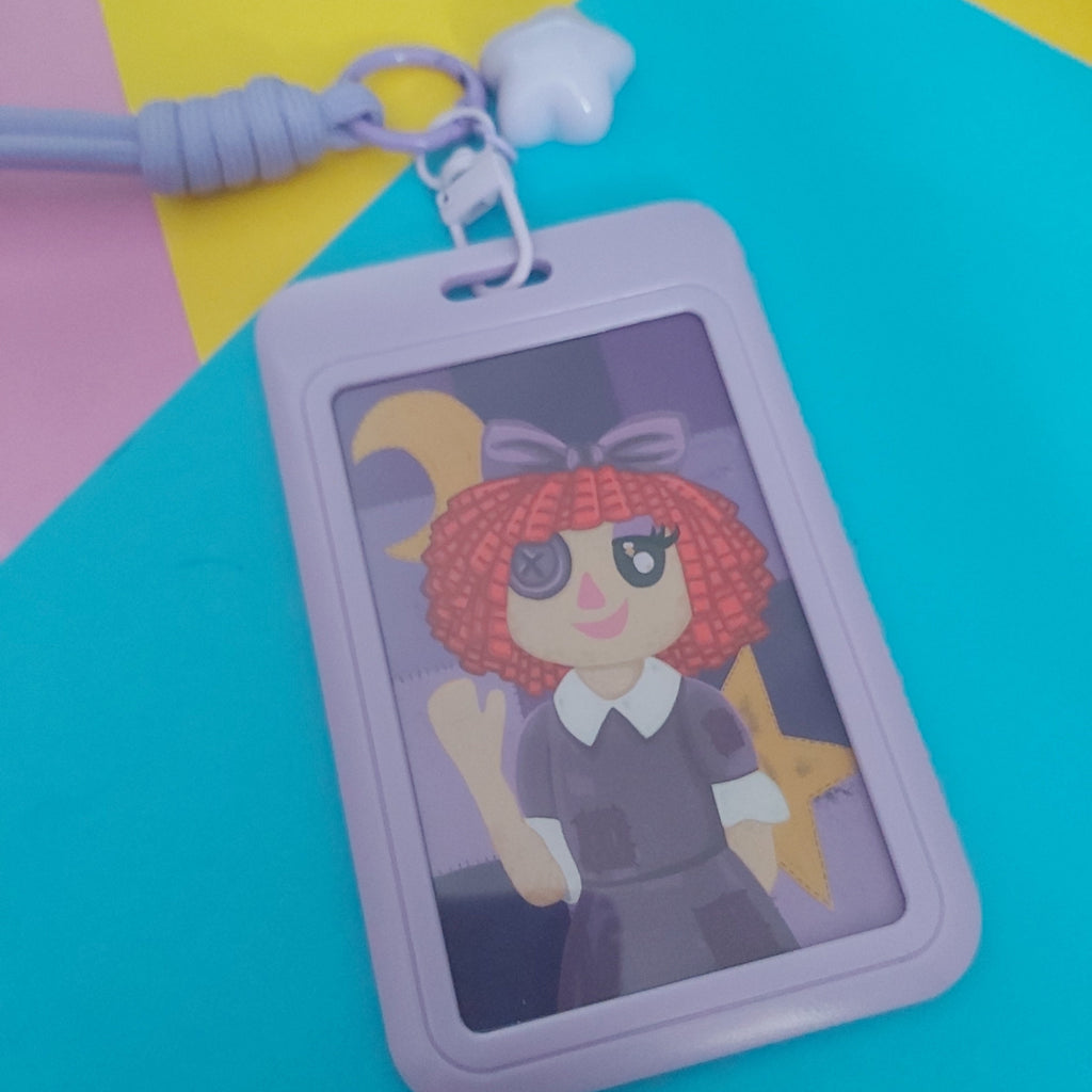 A lavender plastic ID badge holder with a matching wrist strap and star charm, featuring a printed cartoon illustration of a character with red hair. The badge holder is displayed on a colorful background of yellow, pink, and bright cyan paper.