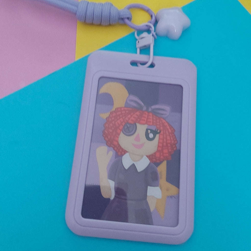 A lavender plastic ID card holder with a matching wrist strap and star charm, featuring a cartoon illustration of a red-haired girl with a purple hair bow. The product is displayed on a colourful background of pink, yellow, and blue paper.