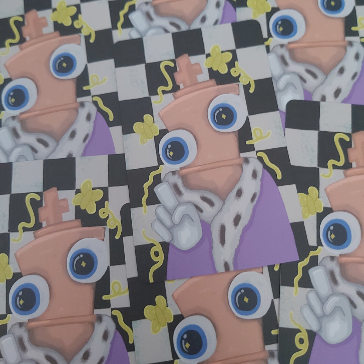 A close-up of a repeating printed pattern featuring a cartoon character with large blue eyes, a peach chess piece body, a purple outfit, and a black-and-white checkerboard background with small yellow motifs.