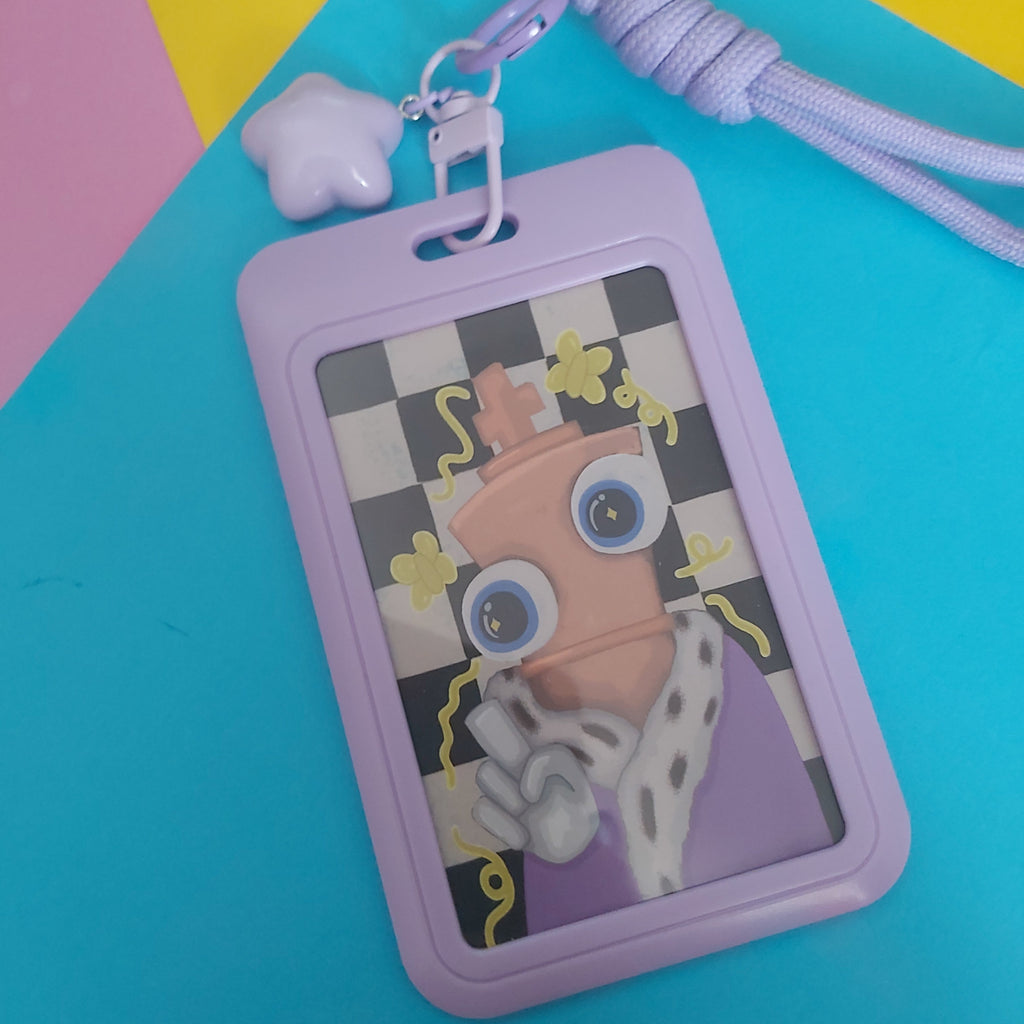 A lavender plastic ID badge holder keychain featuring a stylized cartoon character with large blue eyes, set against a colorful background of cyan, yellow, and pink geometric shapes.