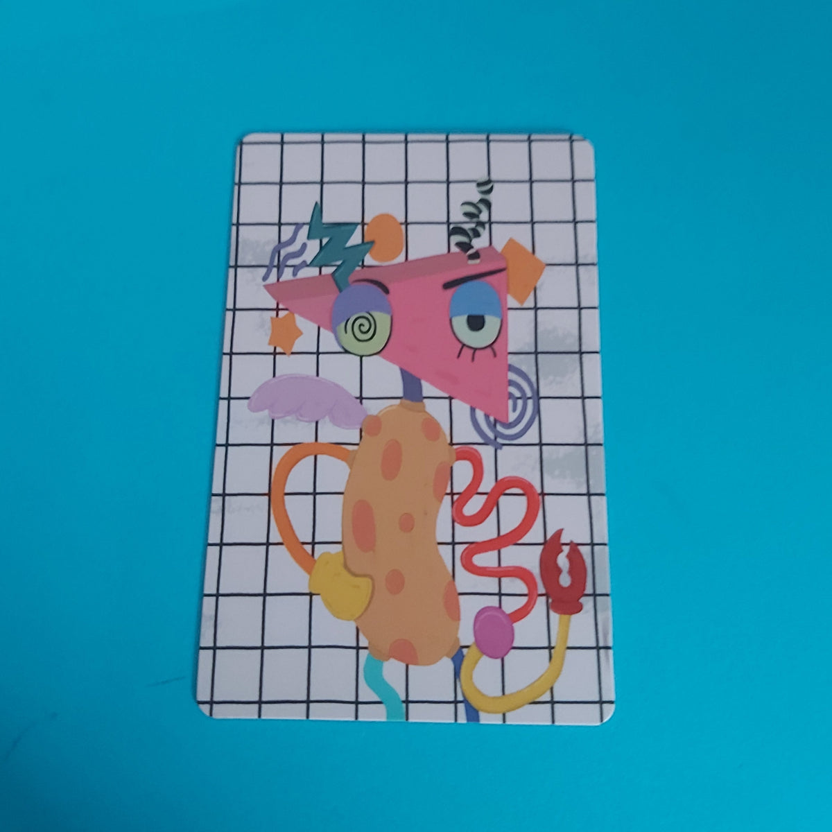 A rectangular art print featuring a colorful abstract cartoon character on a white grid background, placed on a bright blue surface.