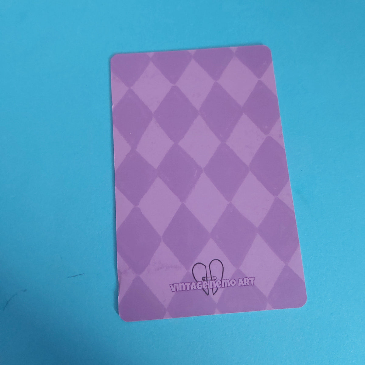 A purple argyle-patterned card with rounded corners, featuring a small heart logo and the text 'VINTAGE NEMO ART' at the bottom, placed on a bright blue background.