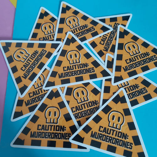 A pile of triangular stickers with a black and orange hazard pattern, featuring a white skull icon and the text 'CAUTION: MURDERDRONES' on a bright blue background.