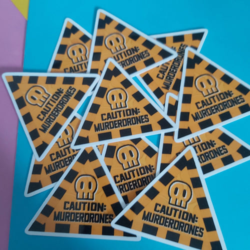 A group of triangular stickers with a black and orange hazard pattern, featuring a skull icon and the text 'CAUTION: MURDERDRONES' on a bright blue background.