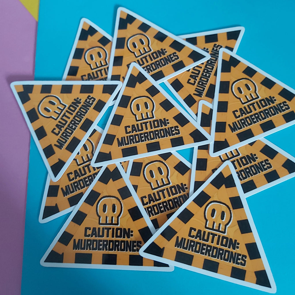 A pile of triangular stickers with a black and orange hazard stripe pattern, featuring a skull icon and the text 'CAUTION: MURDERDRONES' on a bright blue background.
