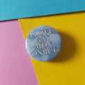A round pinback button with a light blue icy background and raised silver text reading 'I LOVE GAY MEN ON ICE,' placed on a colourful background of pink, yellow, and blue paper.